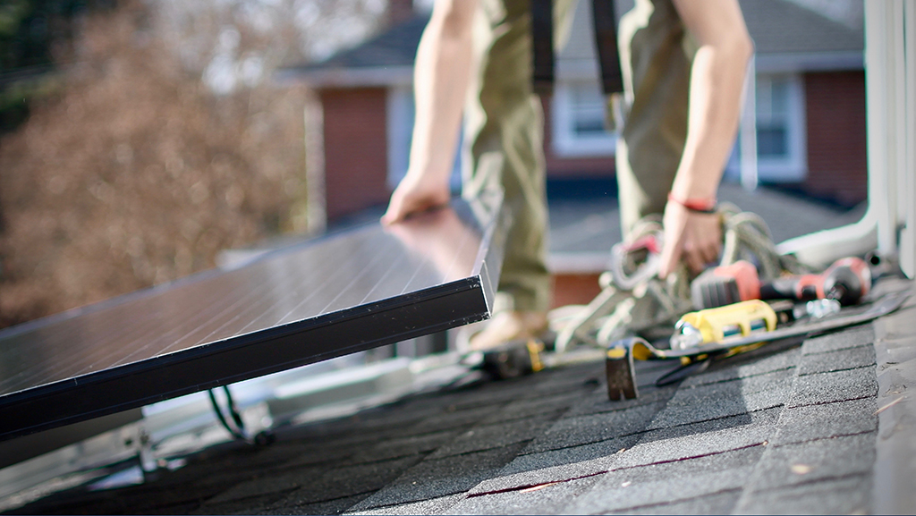 A worker from Sigora Solar installs PV panels on the rooftop of the Heins home.