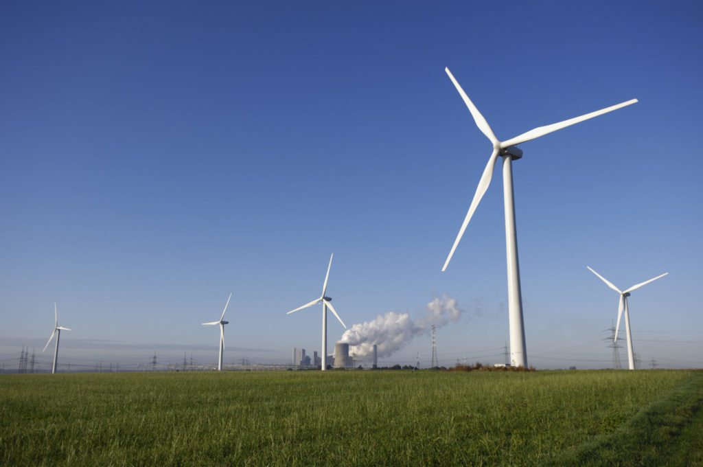 A wind farm operates near a coal-fired power plant. Over the past decade, utility-scale clean energy output has grown by 18.6% per year on average, and the movement toward securing 100% of energy from renewables has grown dramatically: across the country, utilities, corporations, cities, counties, and states are pledging to go 100% renewable.